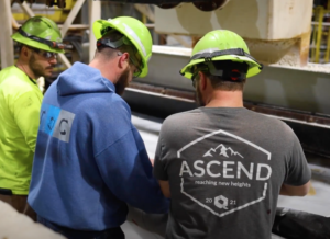 Three employees working together and leaning over an industrial machine