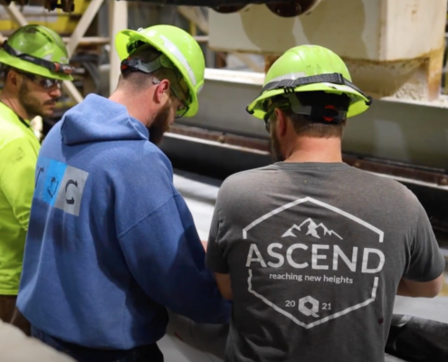 Three employees working together and leaning over an industrial machine