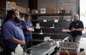 a group of employees standing together in a warehouse as one employee talks to them