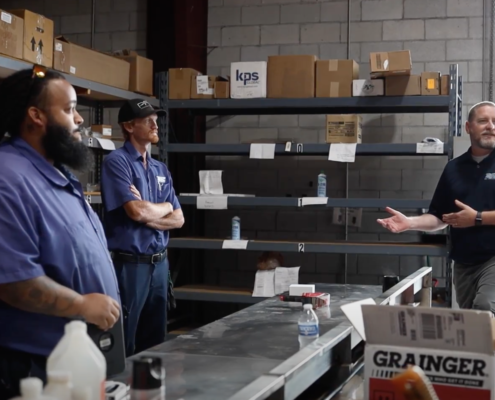 a group of employees standing together in a warehouse as one employee talks to them